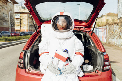 Female astronaut in space suit sitting in car trunk during sunny day