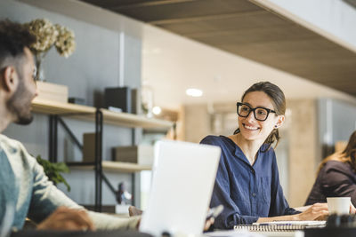 Smiling businesswoman looking at coworker while working in creative office