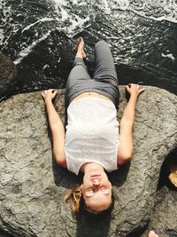 High angle view of young woman lying on rock by sea