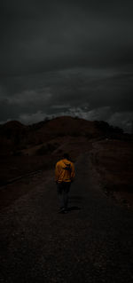 Rear view of man walking on landscape against sky