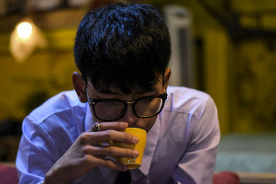 Man wearing eyeglasses while drinking coffee indoors