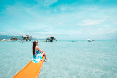 Smiling woman sitting on boat sailing in sea against cloudy sky