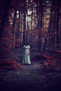 Woman standing amidst trees at forest during autumn