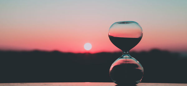 Close-up of clock on glass against sky during sunset