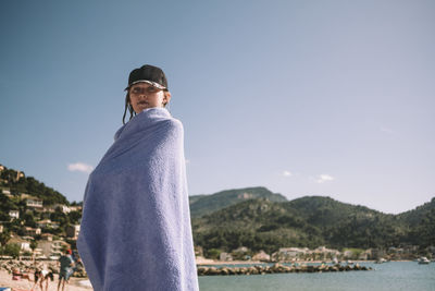 Portrait of girl wrapped in towel standing at beach against sky