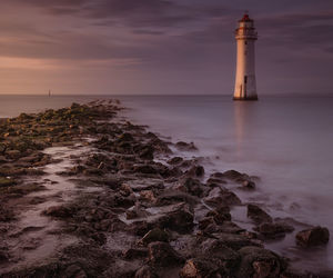 Lighthouse by sea against sky during sunset