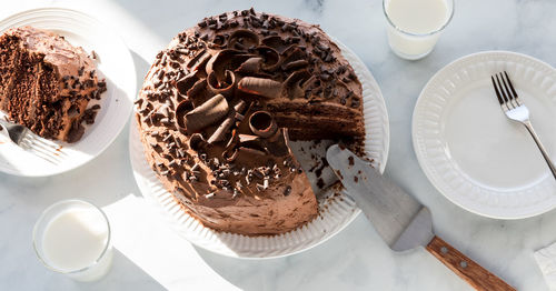 A chocolate cake decorated with chocolate curls with one slice to the left.