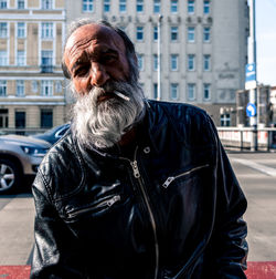 Portrait of bearded man smoking cigarette against building in city