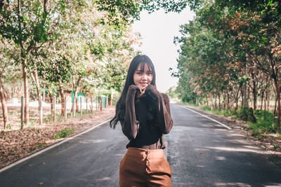 Portrait of young woman standing on road against trees