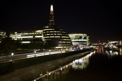 Illuminated buildings by river against sky in city at night