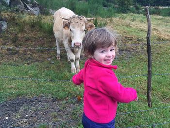 Rear view portrait of happy girl standing by fence against cow on field