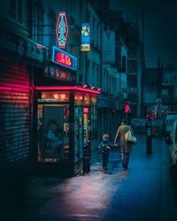 Rear view of people walking on illuminated street at night