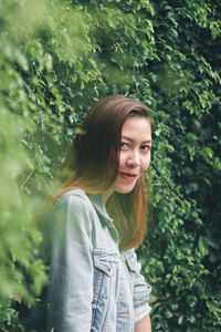 Portrait of smiling young woman standing against plants