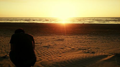 Rear view of a person sitting on calm beach