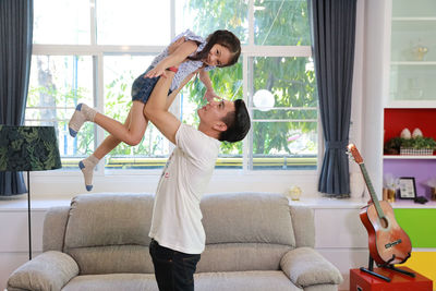 Side view of father holding daughter midair at home