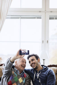 Happy man taking selfie with young caretaker in nursing home