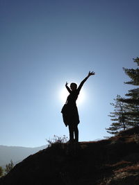 Low angle view of silhouette woman with standing on cliff against clear blue sky