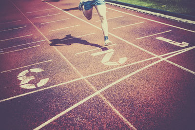 Low section of man running on sports track during sunny day