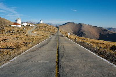 Road leading towards mountains against blue sky