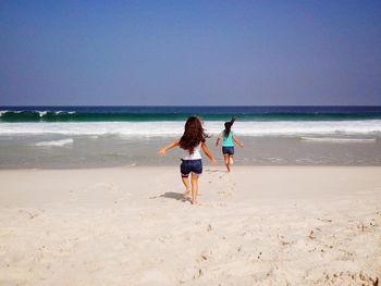 Rear view of sisters on beach against sky