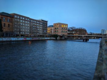 Bridge over river by buildings against clear sky