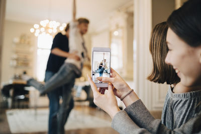 Girl photographing teenage boys through mobile phone dancing at home