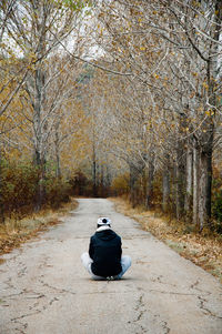 Rear view of man sitting on road in forest