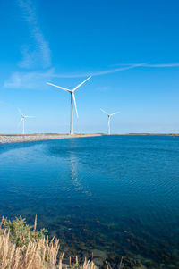 Wind turbines in sea against blue sky