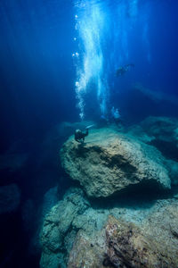 People scuba diving by rocks at undersea