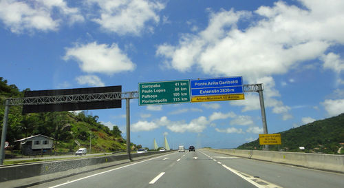 Road sign by highway against sky