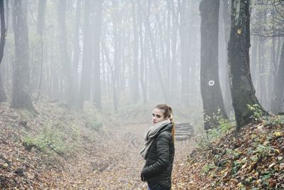 Side view portrait of woman standing in forest during foggy weather