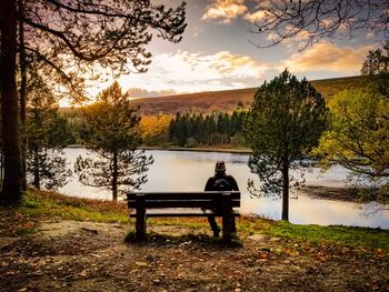 Man sitting on bench by river against sky