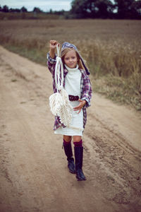Blonde girl in white in a dress and boots goes with a dream catcher in a wheat field