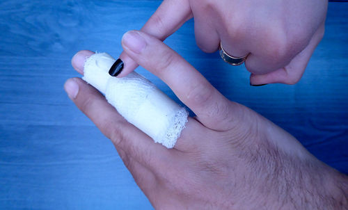 Cropped hand of man with bandage on finger by woman over table