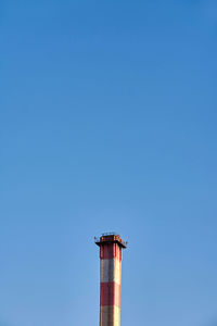 Low angle view of smoke stacks against clear blue sky