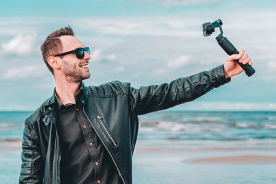 Man wearing sunglasses standing by sea against sky