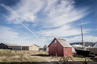 Barn on field by houses against sky