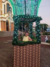 Portrait of woman sitting on plant against building