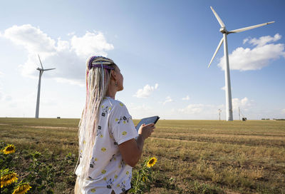 Young woman with tablet in field sunflowers, wind turbines for green energy production, eco-energy