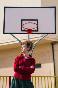 Low angle view of young woman standing by basketball hoop