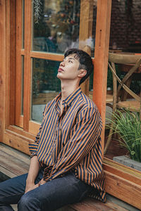 Young man looking away while sitting on wood