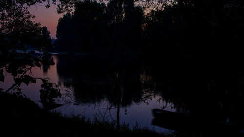 Silhouette trees by lake against sky at sunset