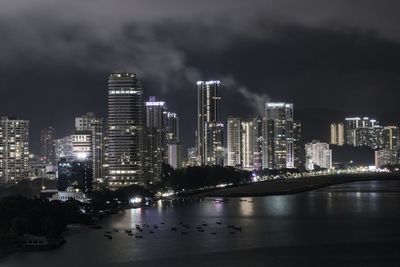 Illuminated city by sea against sky at night