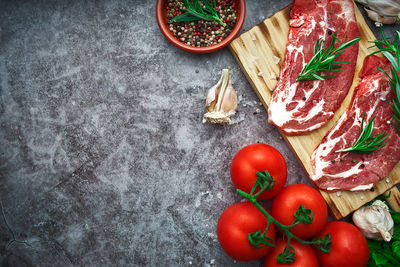 Raw beef steak with tomato, garlic, pepper, salt and rosemary on frying pan on a dark background.