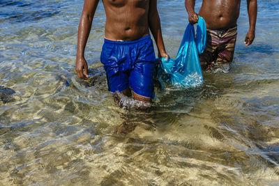 Midsection of fishermen carrying net in sea