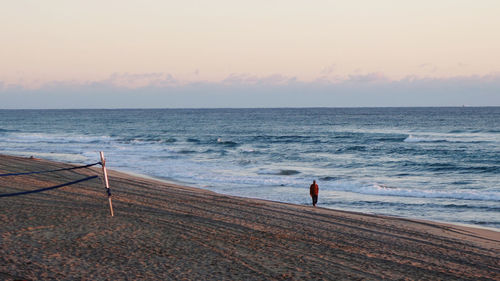 Rear view of man standing on beach against sky during sunset