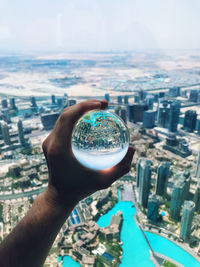 Close-up of hand holding cityscape against sky in city