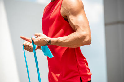 Midsection of man holding resistance bands while standing against wall in gym