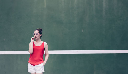 Woman wearing eyeglasses while standing against wall