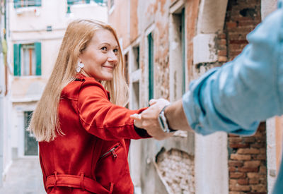 Side view of a smiling young woman standing against building in city